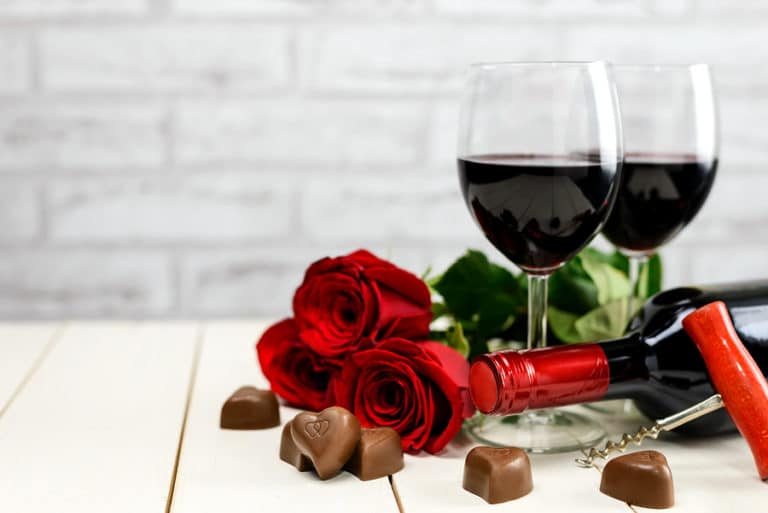 Valentine's Day at a Bainbridge Island Winery Two glasses of wine, wine bottle, corkscrew, red roses and chocolate hearts on a white wooden table.